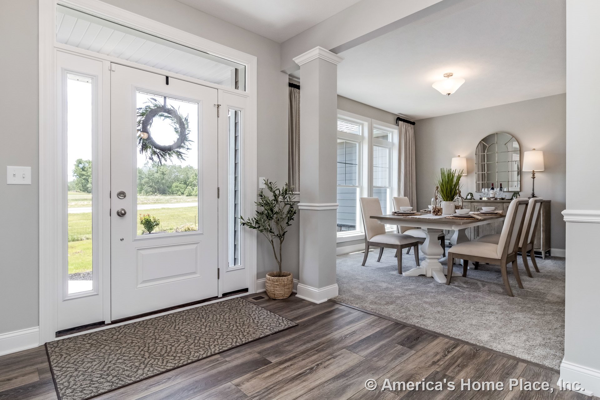 White paneled front door with sidelights opens to foyer with wood-look flooring, transitioning to carpeted dining room featuring large trimmed windows, ceiling light fixture