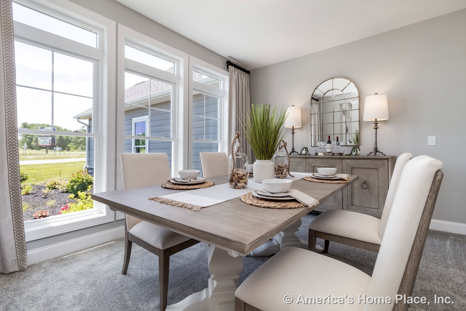 Dining room with three-pane picture windows, light gray carpet flooring, built-in wood buffet cabinet featuring mirrored wall accents, white trim, and ceiling-mounted lighting