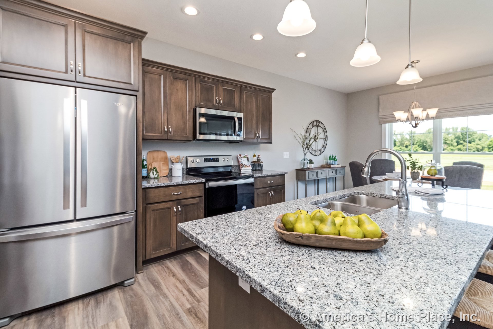 Granite island with undermount sink, stainless steel French door refrigerator, wood upper and lower cabinets, built-in microwave above electric range, pendant and recessed ceiling