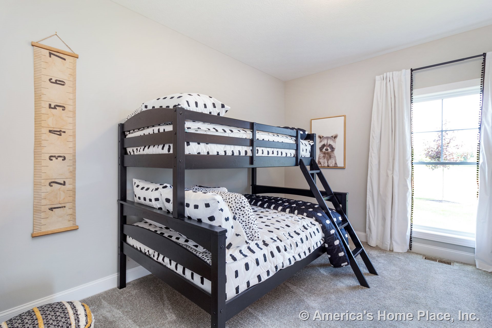 Children's bedroom with neutral walls, carpet flooring, white baseboard and window trim, large window dressed in white curtains, and built-in bunk bed.