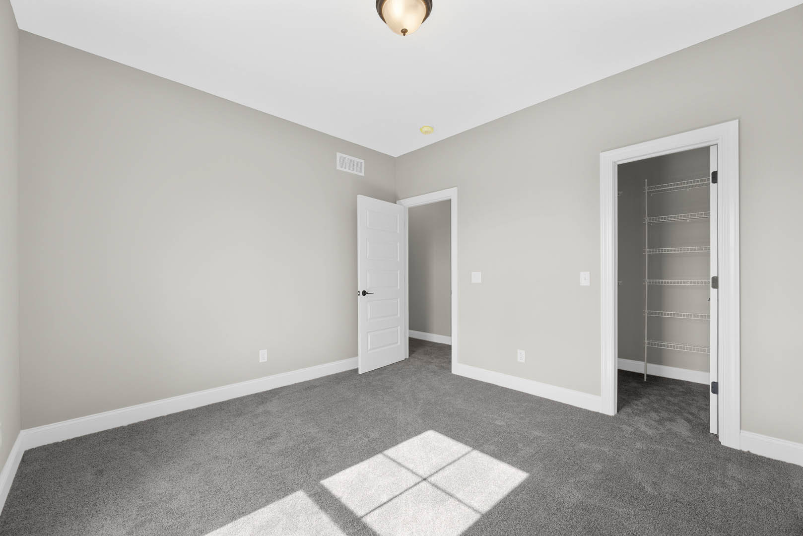White paneled door with black handle opens to a carpeted room featuring a built-in white closet with shelving, recessed ceiling light, and white walls with crown molding.
