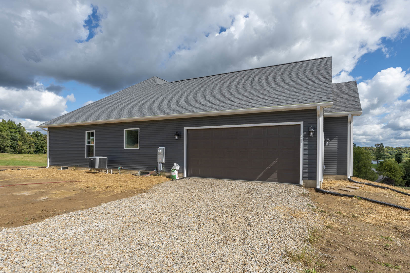 Modern two-story house with light siding, attached garage featuring white paneled door, paved driveway, large front window, landscaped yard with gravel border, central air