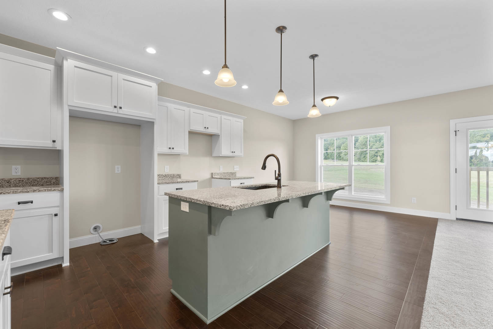 Open kitchen with wood flooring, central island featuring built-in sink and faucet, white cabinetry, tile backsplash, large window overlooking outdoors, and white door with glass
