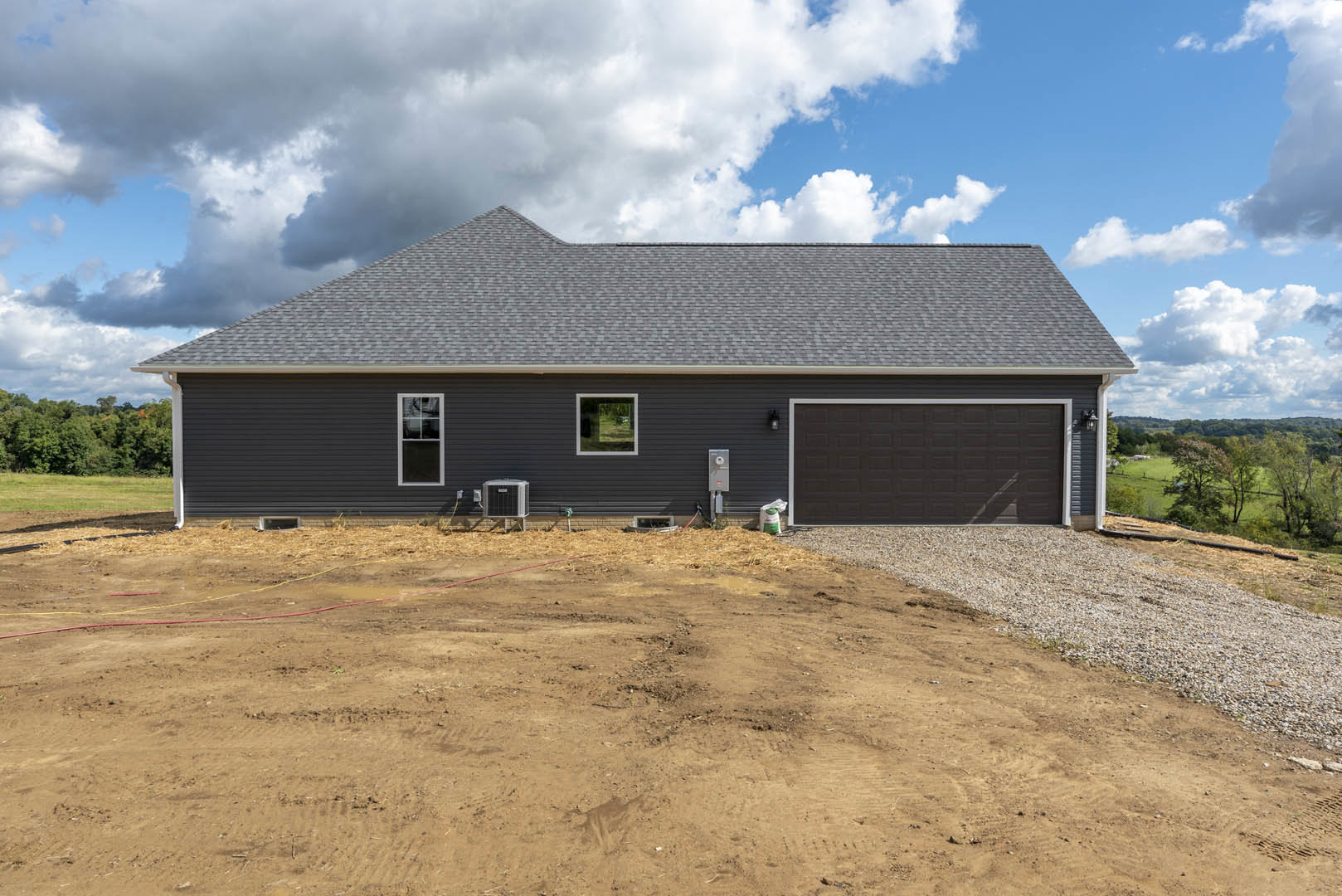 Modern home with black garage door and white trim, large front window, concrete driveway, dirt yard, and cloudy sky