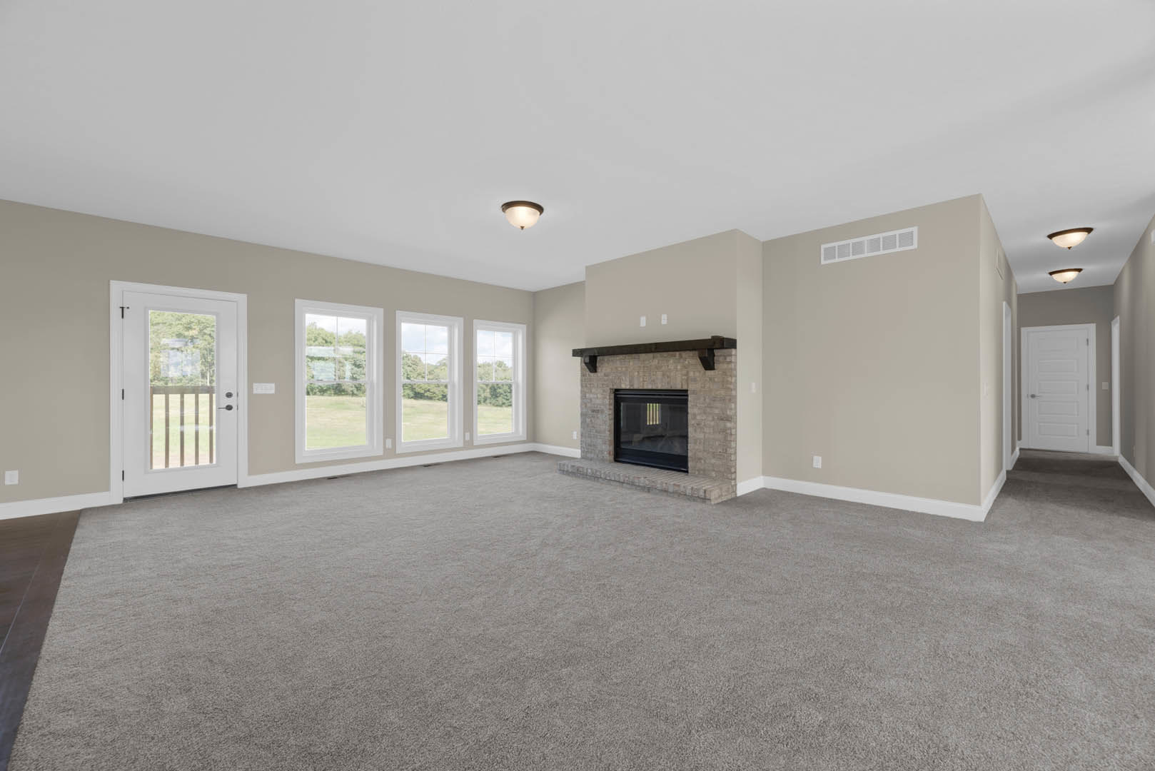 Carpeted living room featuring a brick fireplace with glass doors, large window, white door with silver knobs and glass panes, plaster walls, and laminate flooring.