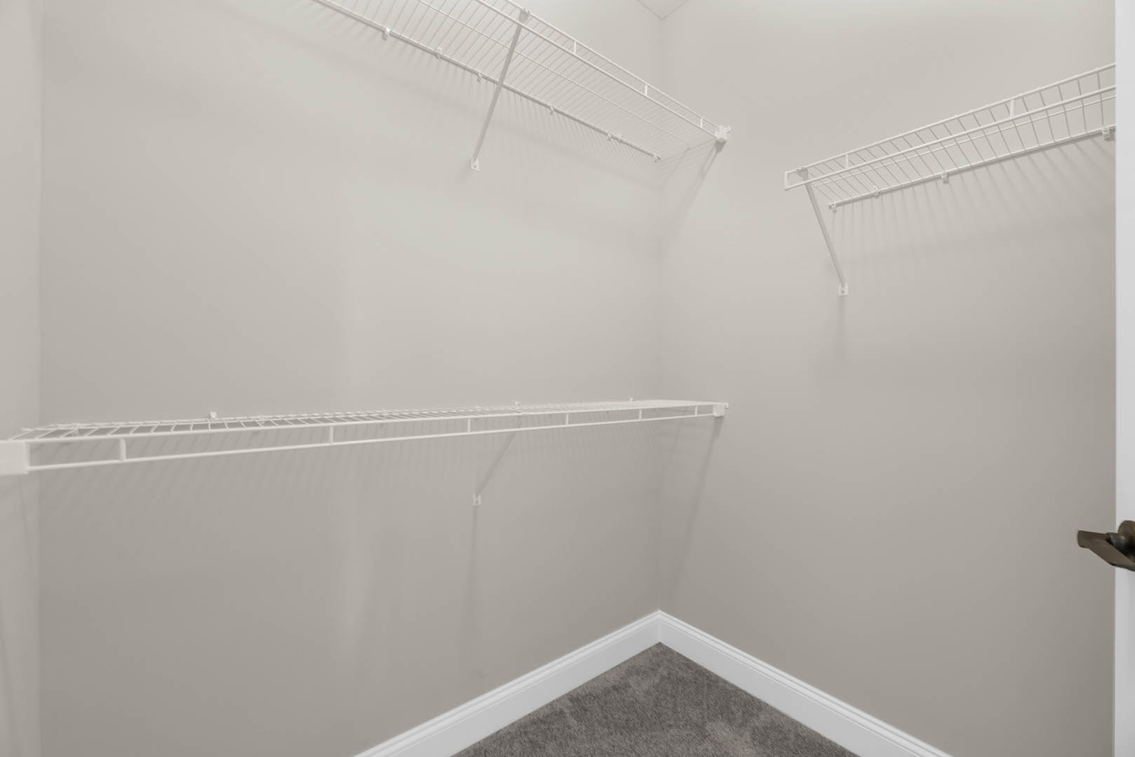 Corner of a carpeted room with built-in white shelves on a white wall, metal shelf supports, and tile flooring visible near a bathroom area with a close-up of a chrome faucet.