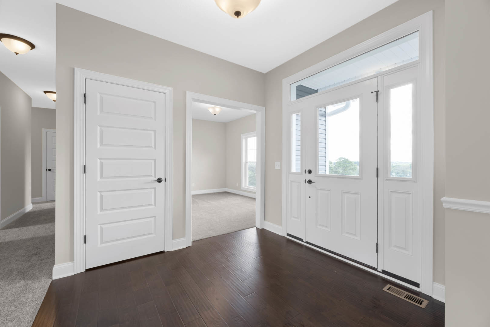 Hallway featuring dark wood laminate flooring, white trim, multiple white doors including a double door with glass panes, white walls, ceiling vent, and a window in an adjacent