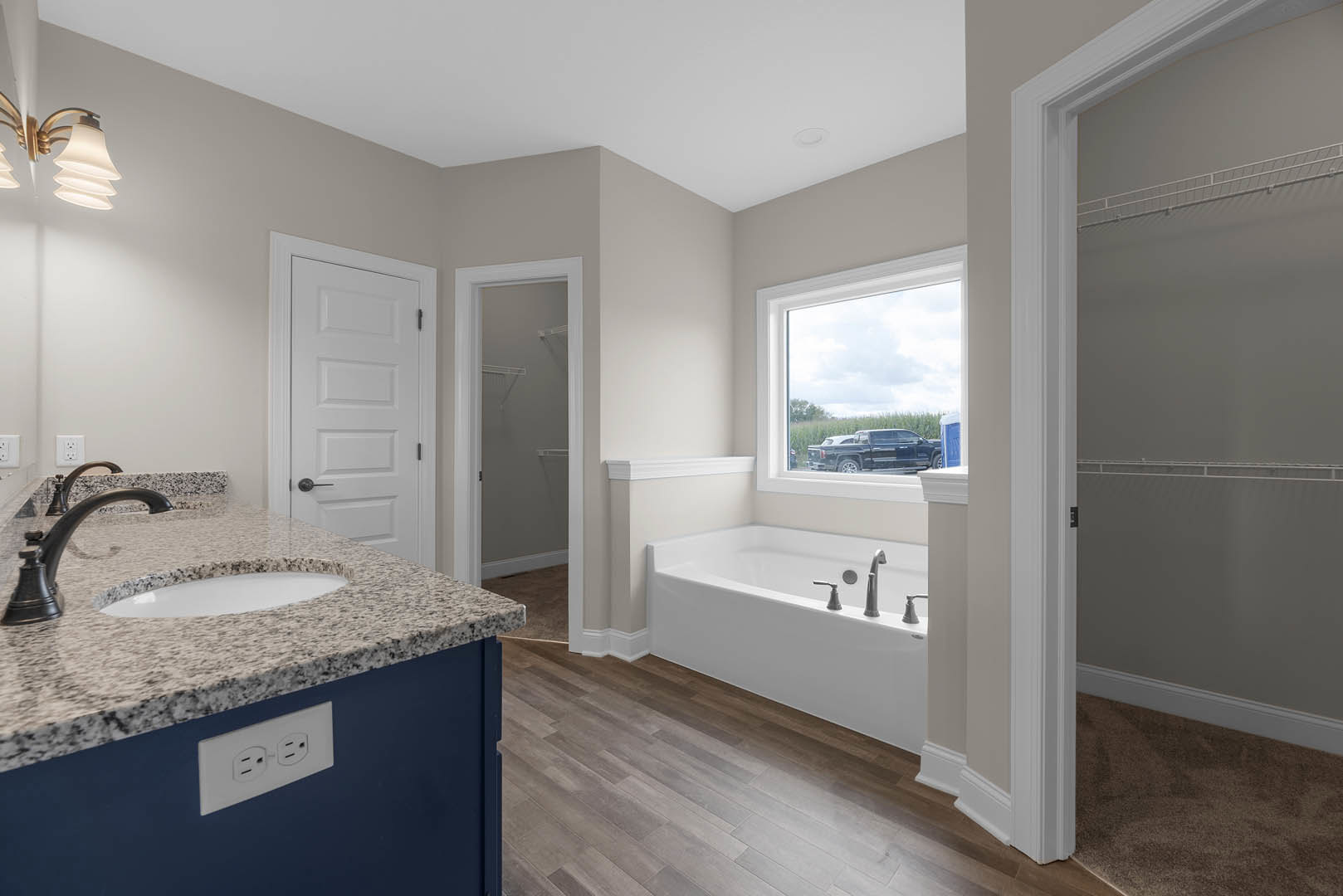 Bathroom with freestanding bathtub, white vanity with undermount sink and chrome faucet, large wall mirror, light gray tile flooring, and white door with black handle