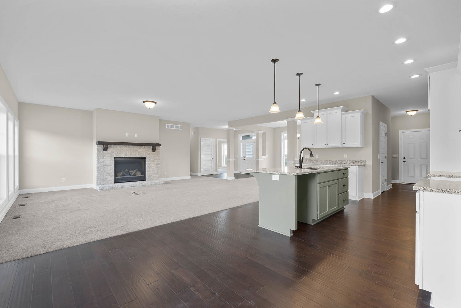 Spacious open floor plan featuring hardwood floors, central kitchen island with white cabinetry and sink, modern fireplace with glass door, white doors with black handles, recessed
