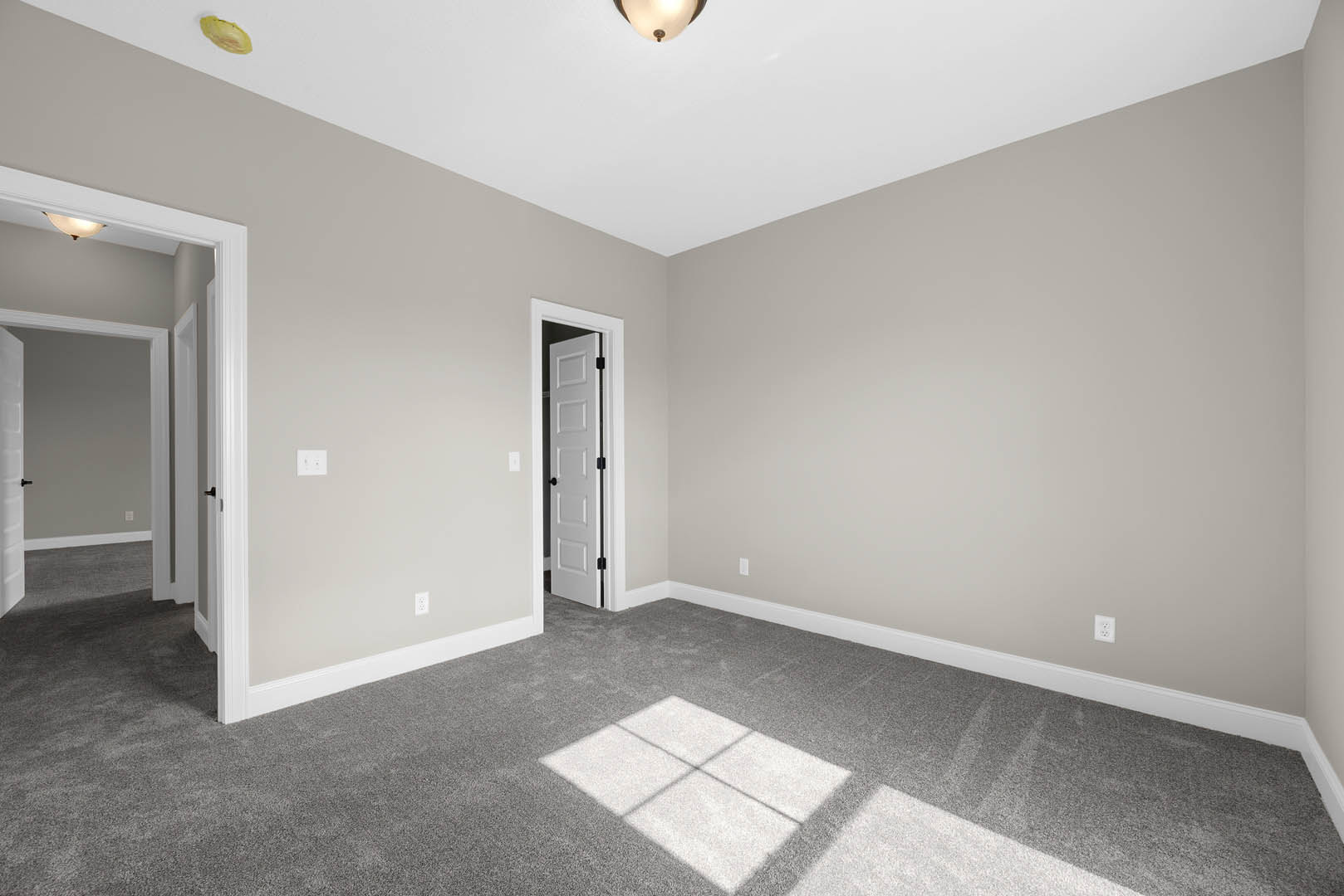 White paneled door with black handles opening into a carpeted room, ceiling light fixture illuminating neutral walls and white baseboards.