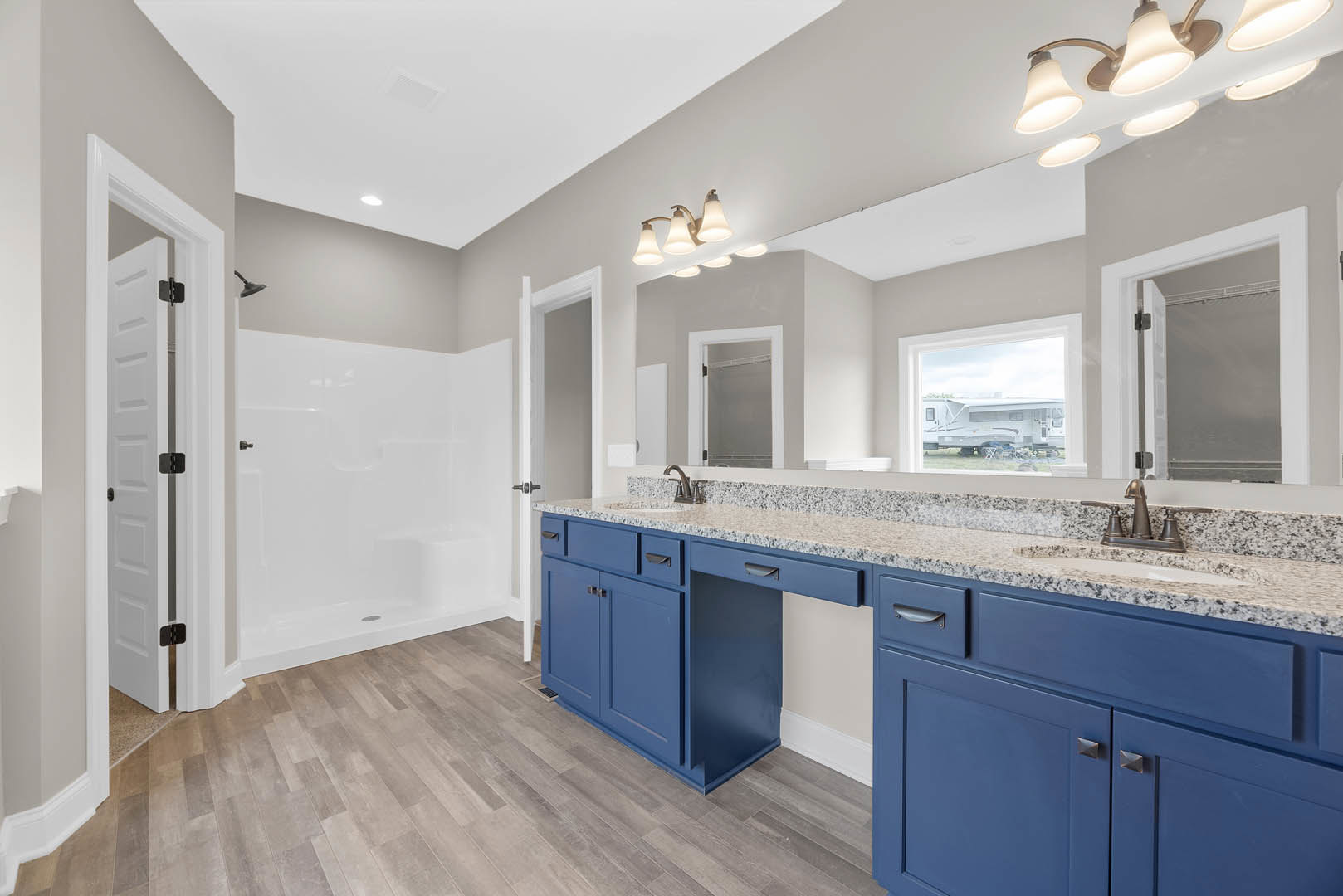 Bathroom with blue cabinetry, marble countertops, white tile shower, wood flooring, white door with metal hinge, and modern light fixture