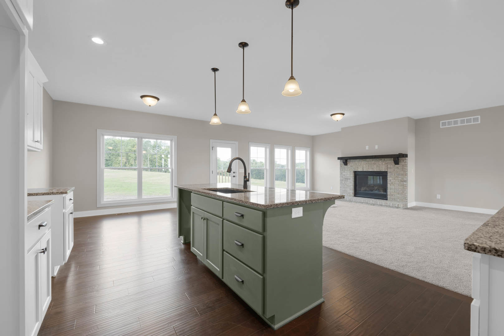 Kitchen with marble-topped island, brick fireplace with black glass window, cabinetry, wood flooring, ceiling lights, and large window overlooking grassy field