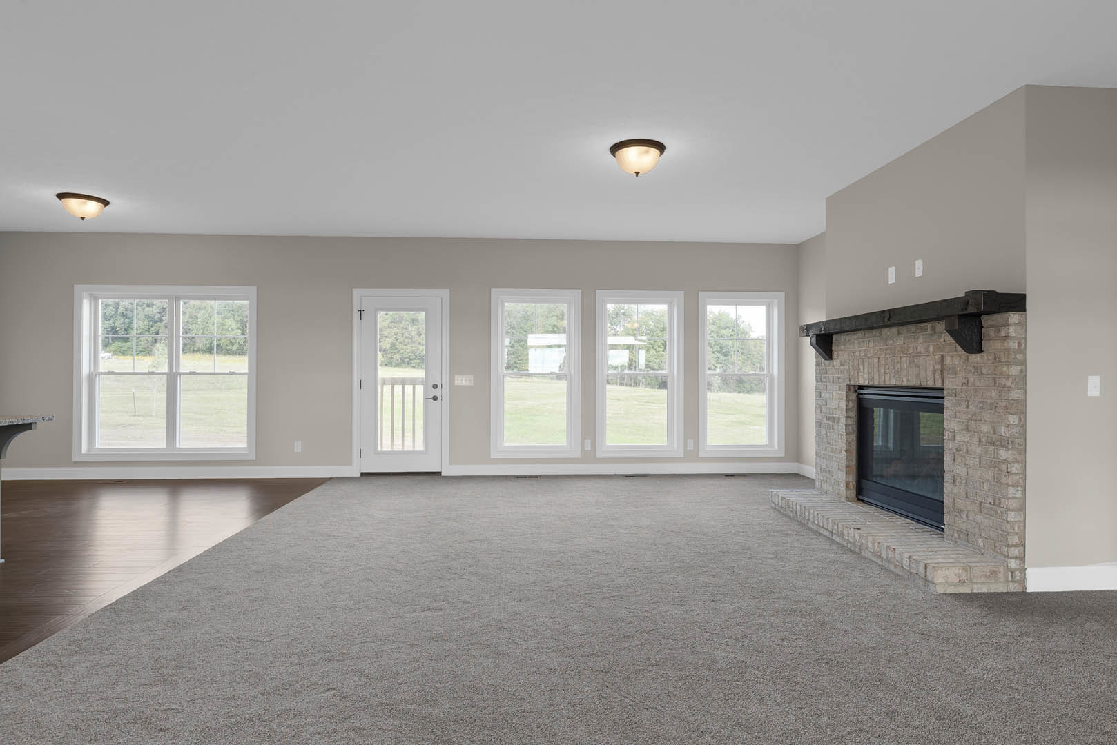 Living room with white walls, carpeted floor, central fireplace, large window overlooking grassy field, white glass-paneled door
