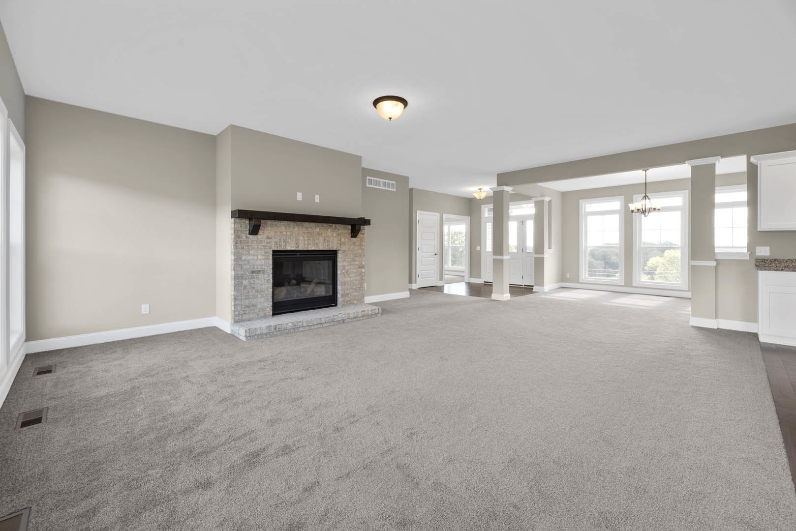 Spacious living room featuring a brick accent wall with glass door, central fireplace, light fixture on plaster ceiling, and hardwood flooring with decorative molding