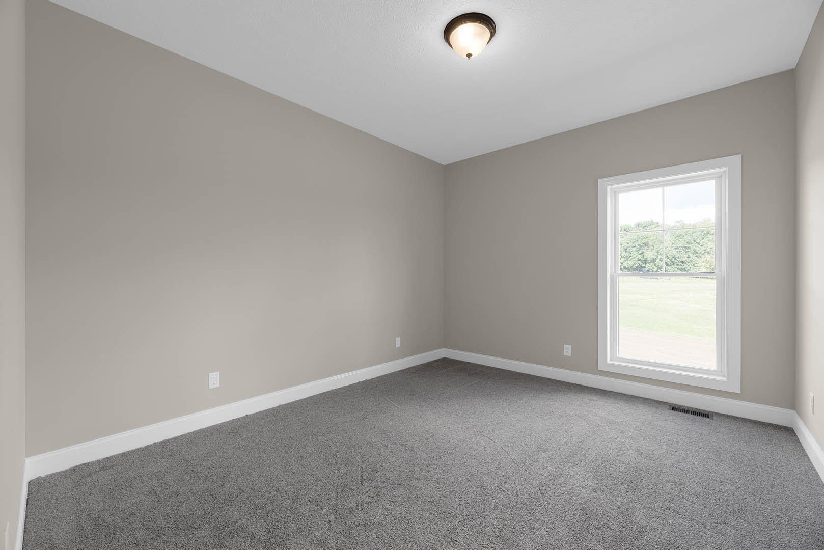 Grey carpeted room with white walls, large window overlooking green trees, and modern ceiling light fixture