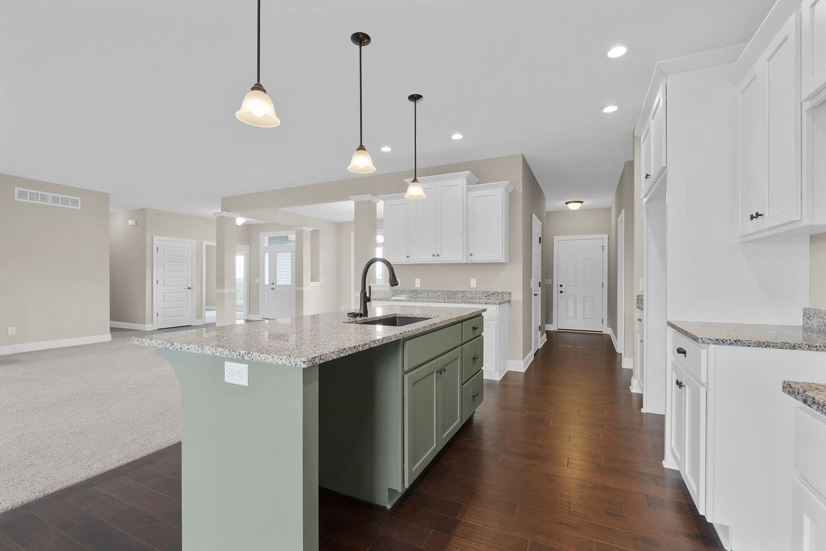 Spacious kitchen featuring a large central island with granite countertops, white cabinetry, stainless steel sink, tile flooring, and a white door with black knobs.