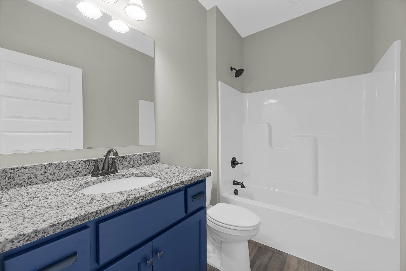 Bathroom with white bathtub, toilet, and sink featuring blue cabinetry, chrome faucet, and tiled walls