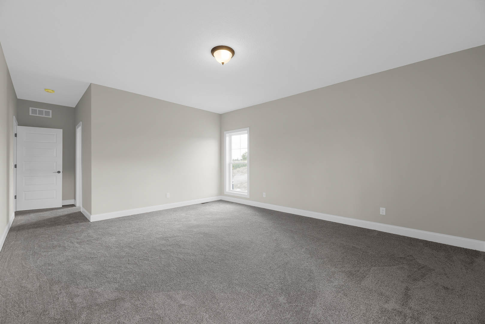 Carpeted room with white walls, ceiling light fixture, white door with black handle, and window overlooking grassy field