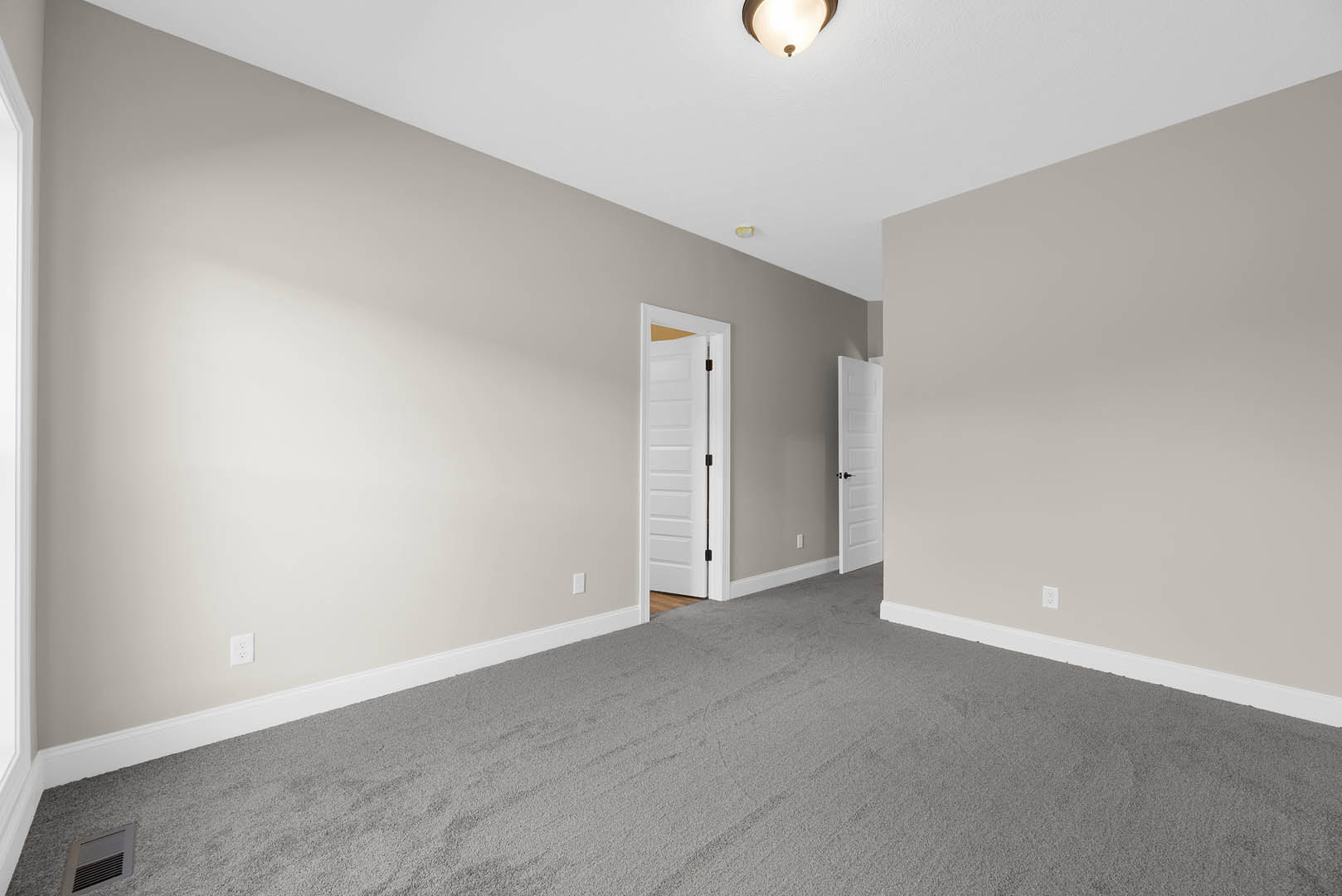 Carpeted room with white walls, white door featuring a black handle, ceiling-mounted light fixture, and floor vent
