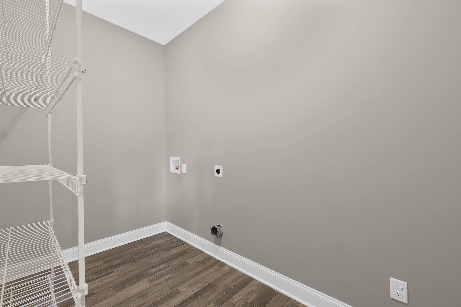Wood plank flooring, smooth white plaster wall with recessed outlet, partial view of white metal handrail and shelf, open stairwell leading to upper floor.