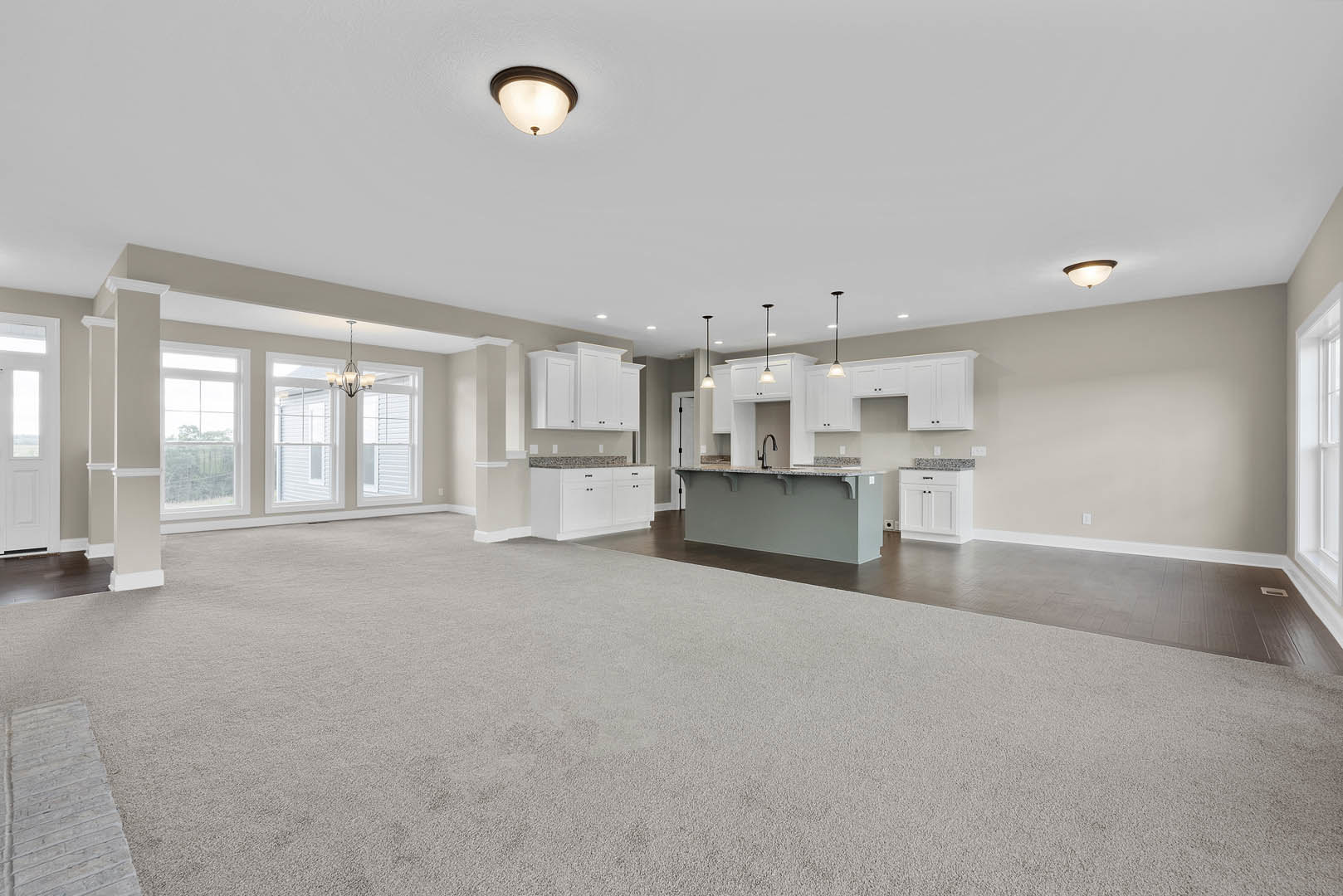 Spacious open floor plan featuring a marbled kitchen island, carpeted flooring, ceiling light fixture, large window with tree views, and a white door with glass inset.