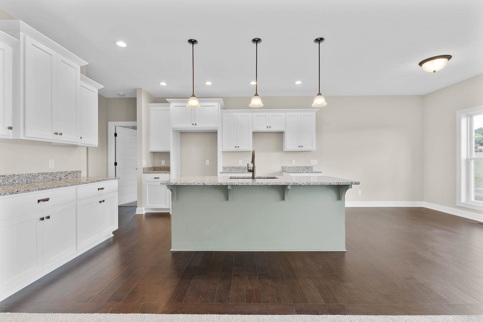 White kitchen cabinets with marble countertops, central island with built-in sink, wooden flooring, open shelving above, large window providing natural light.