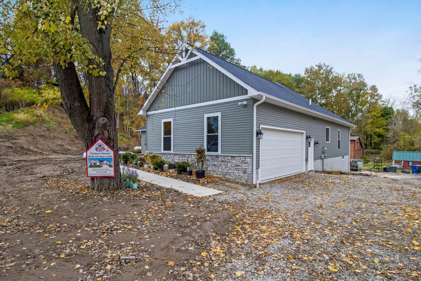 Two-story house with attached garage, white-framed windows, gray siding, and a mature tree in the front yard
