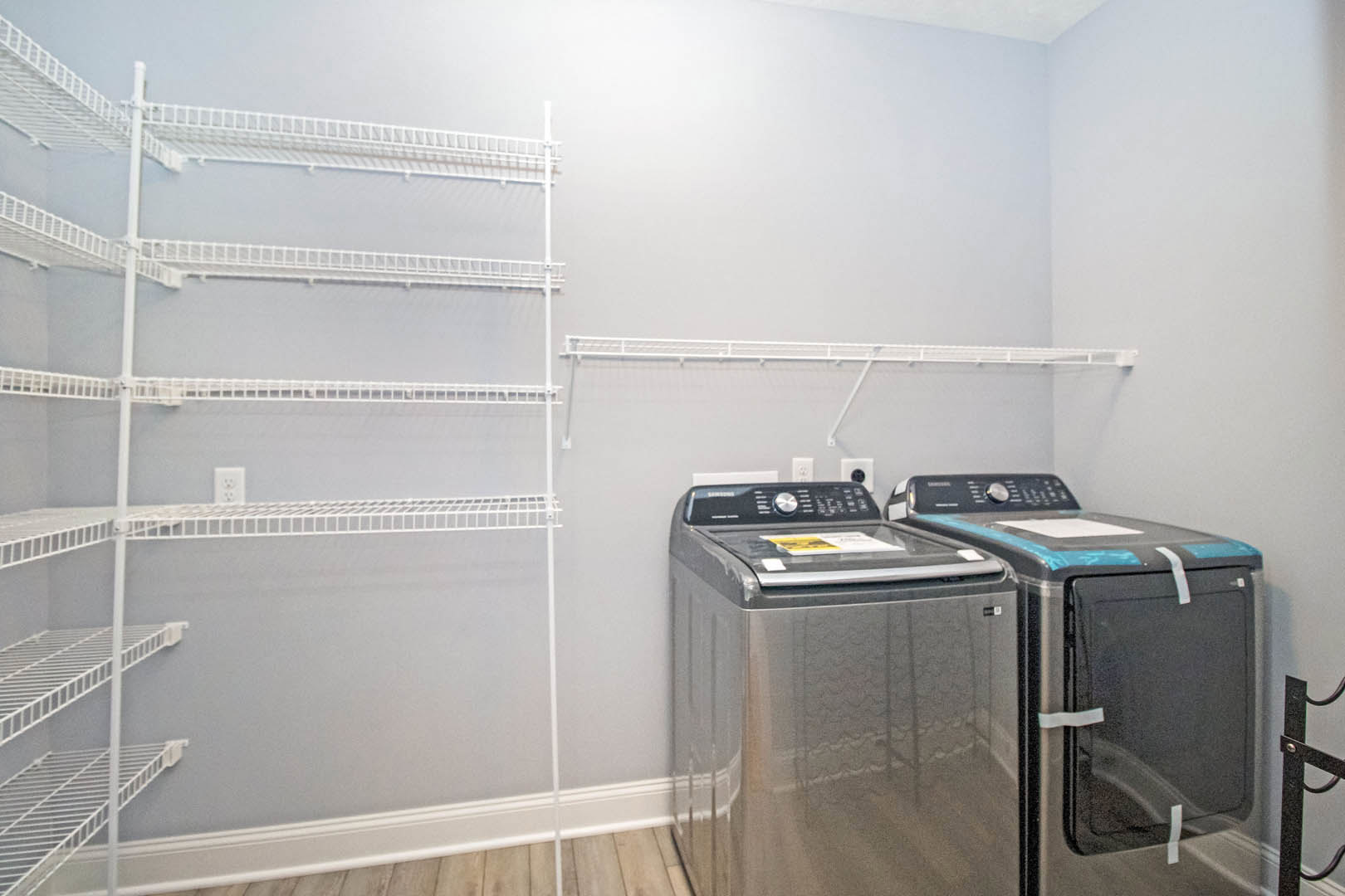 Front-loading washing machine and dryer set against white cabinetry and open shelving in a laundry room with light-colored flooring and metal accents