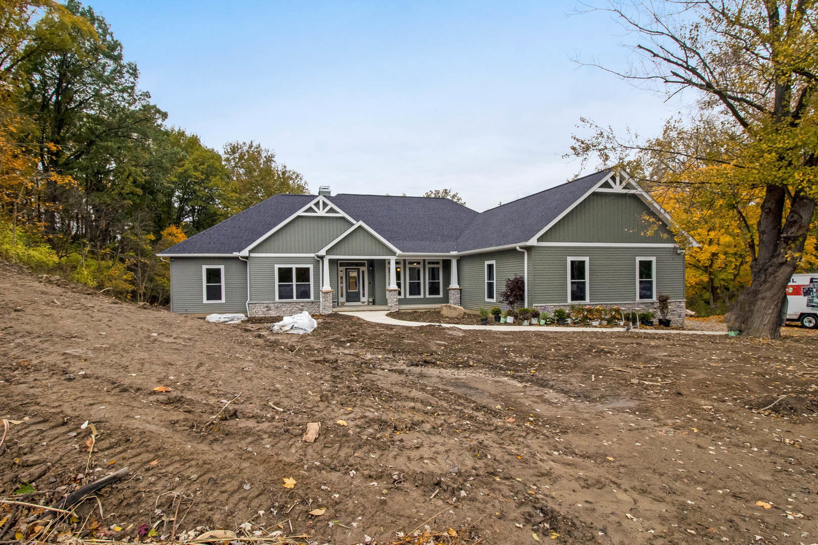 Two-story house with grey roof, white siding, dirt driveway, and a large tree in front