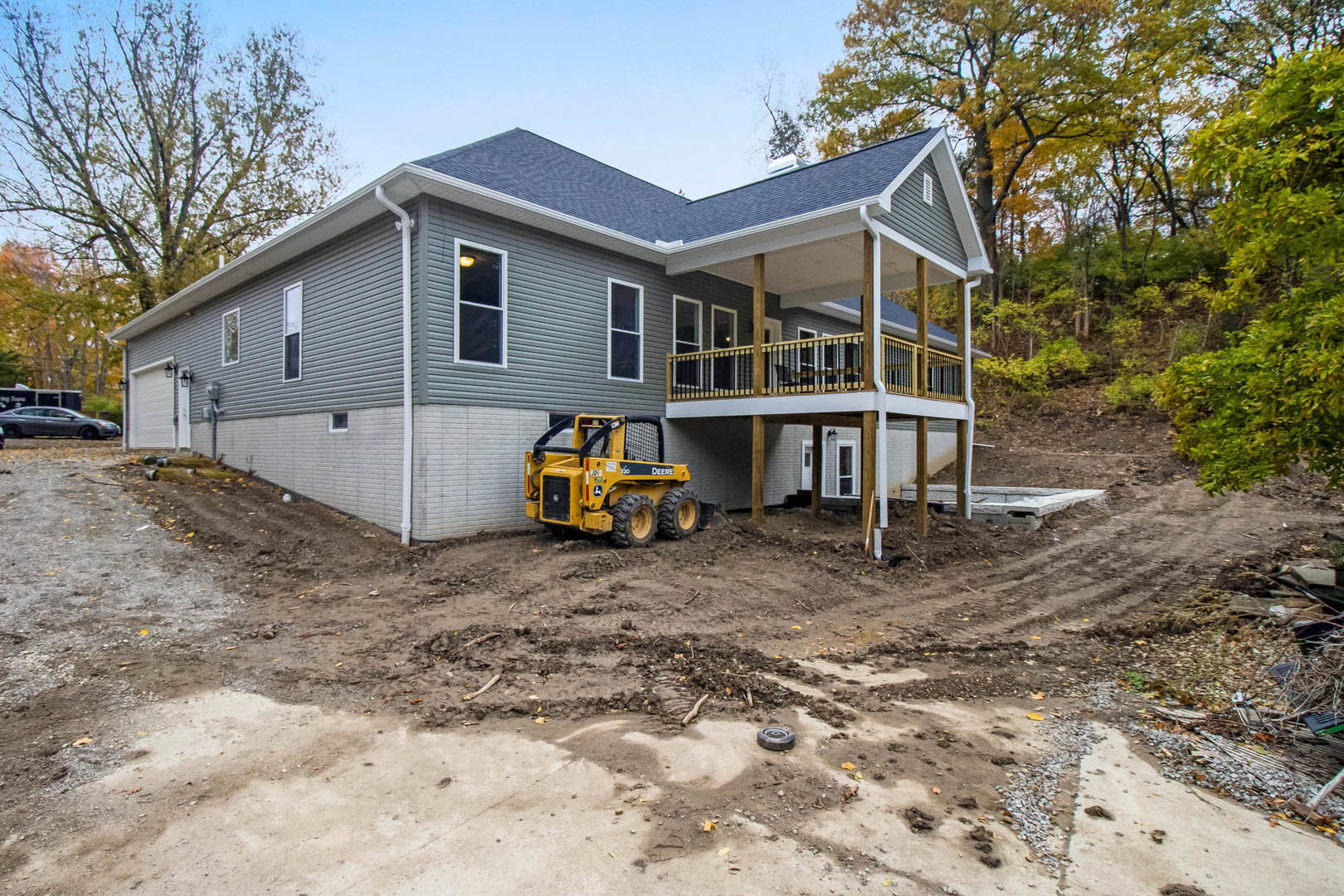 Two-story home with white-framed windows, light-colored siding, and a yellow tractor parked on dirt driveway near mature trees