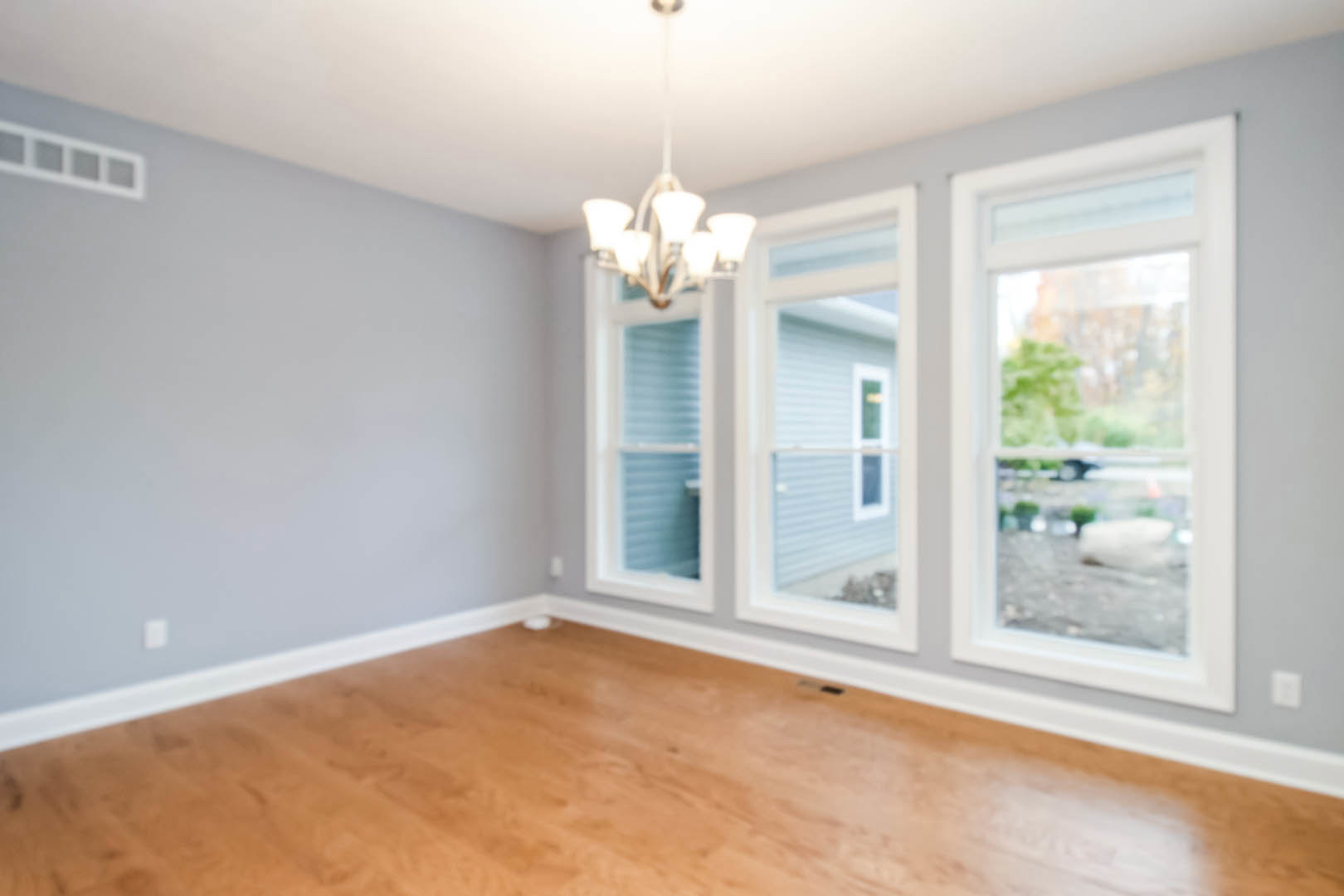 Blurry view of a room with wood flooring, large windows, and a chandelier, with trees and a car visible outside