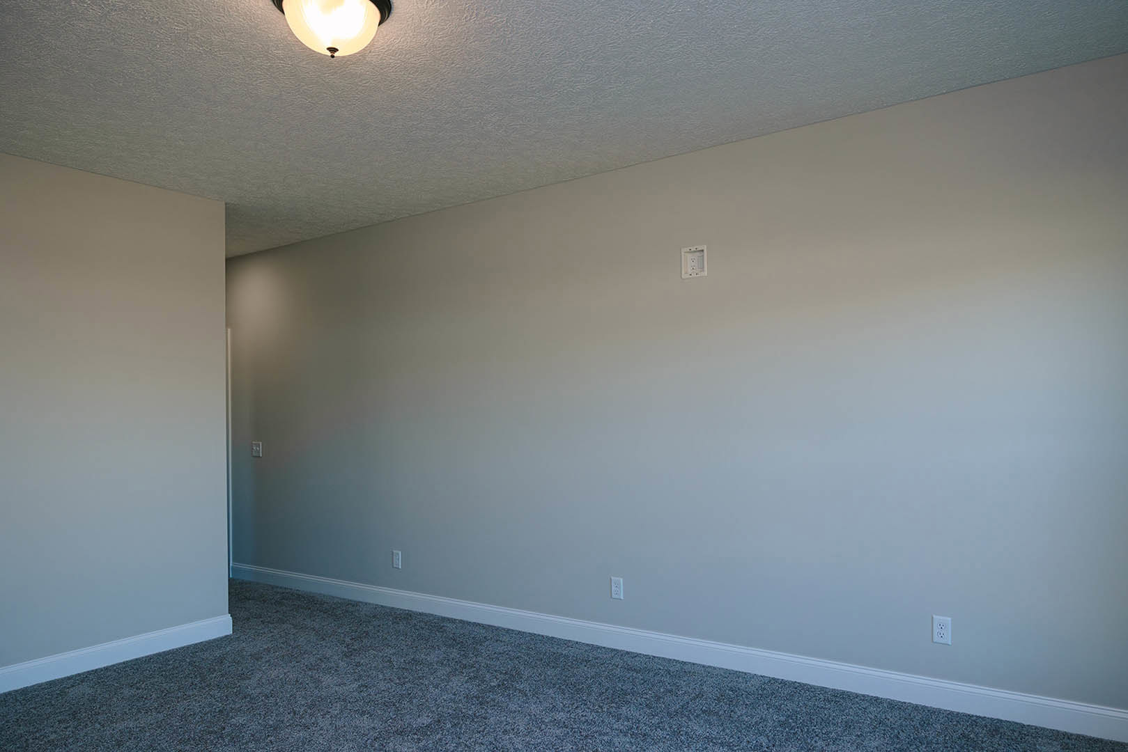 Modern living room with white plaster walls, black trim, neutral carpet flooring, and a ceiling-mounted light fixture illuminated above.