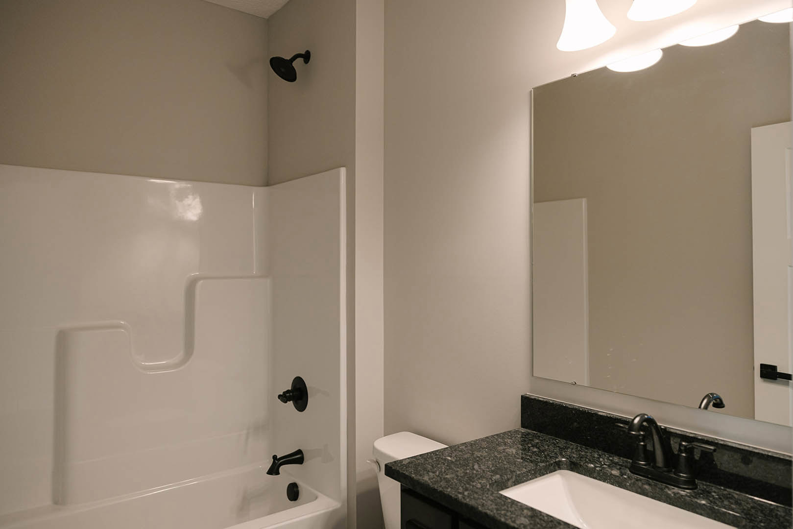 Bathroom featuring a white bathtub with matte black faucets, white tile walls, a modern sink with a black faucet, and a rectangular mirror above the vanity