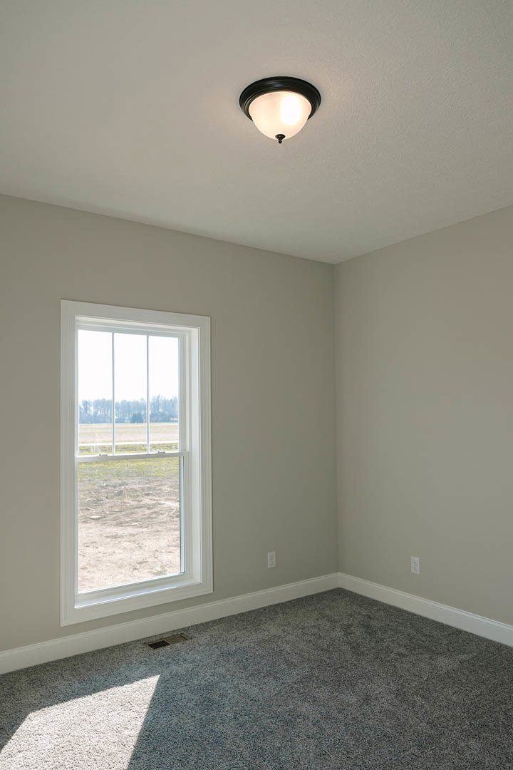 Bedroom with grey carpet, white walls, large window overlooking grassy field, ceiling light fixture, and simple baseboard molding