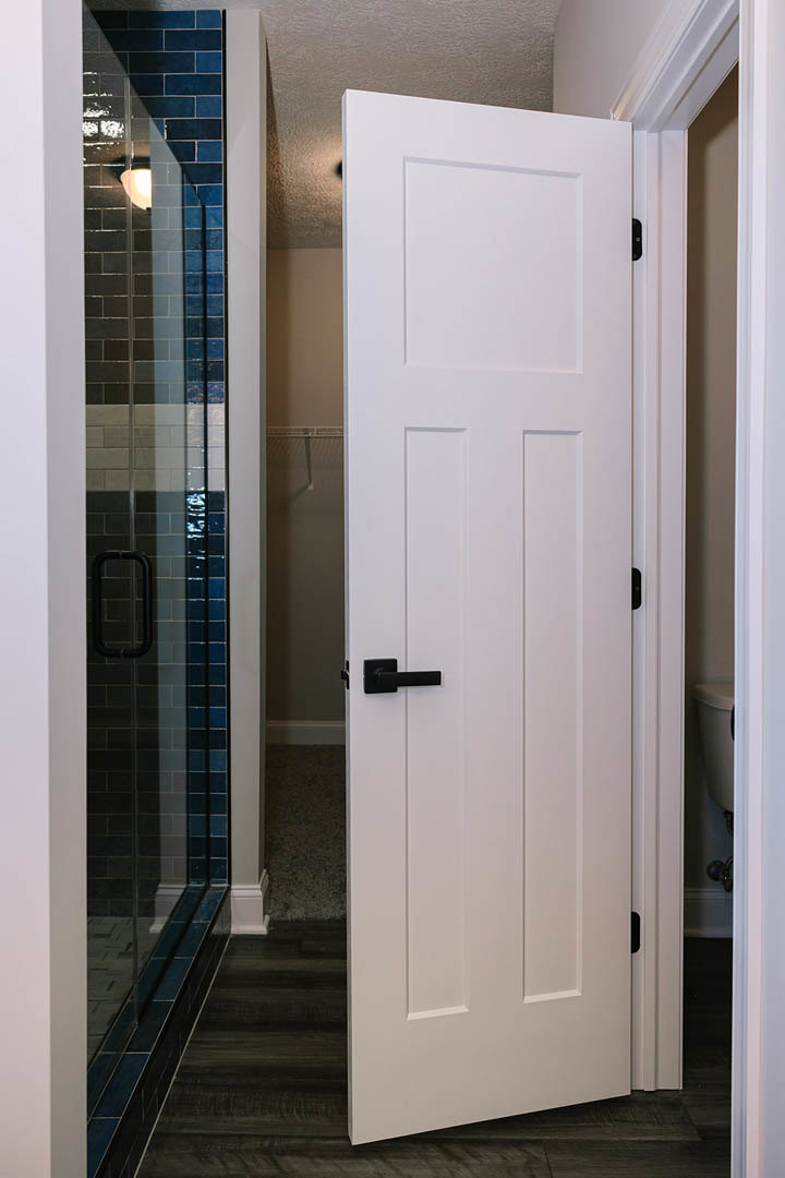 White paneled door with matte black handles set against a light-colored wall and hardwood floor