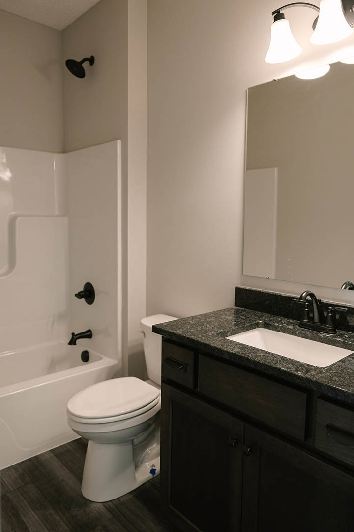 Marble countertop with rectangular white sink, chrome faucet, wall-mounted mirror, white toilet with closed seat, light fixture above, tiled walls