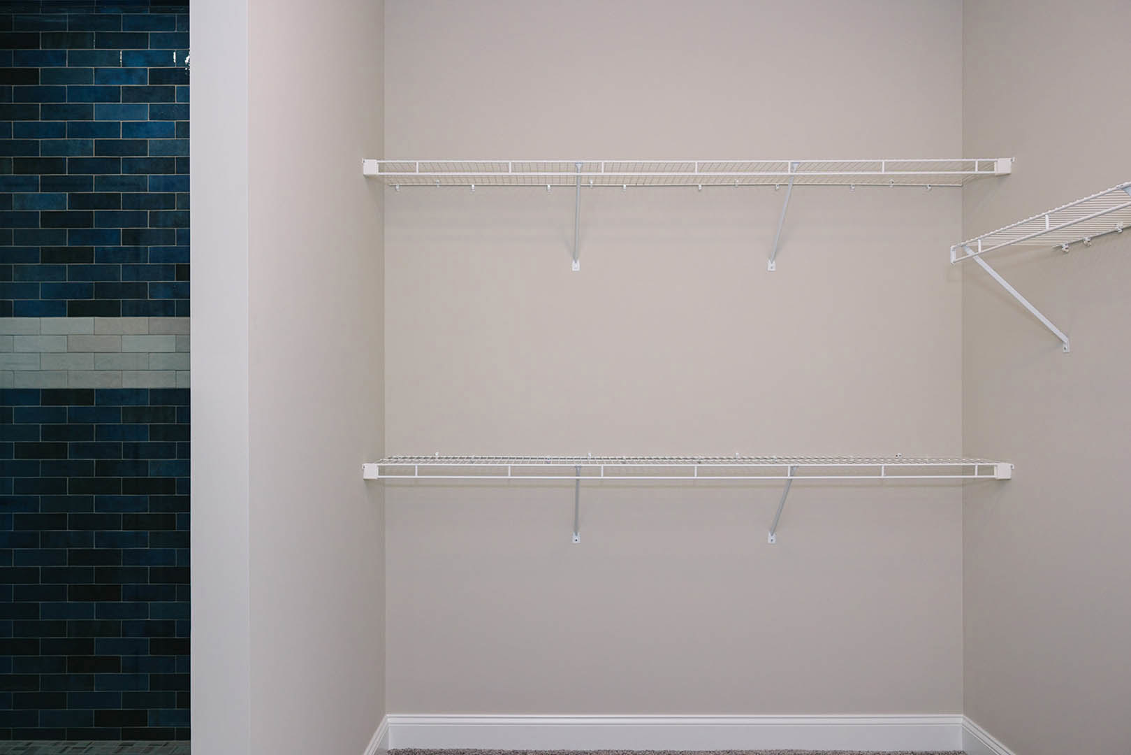 White built-in shelves with hooks mounted on a plaster wall in a bathroom, adjacent to tiled shower area.