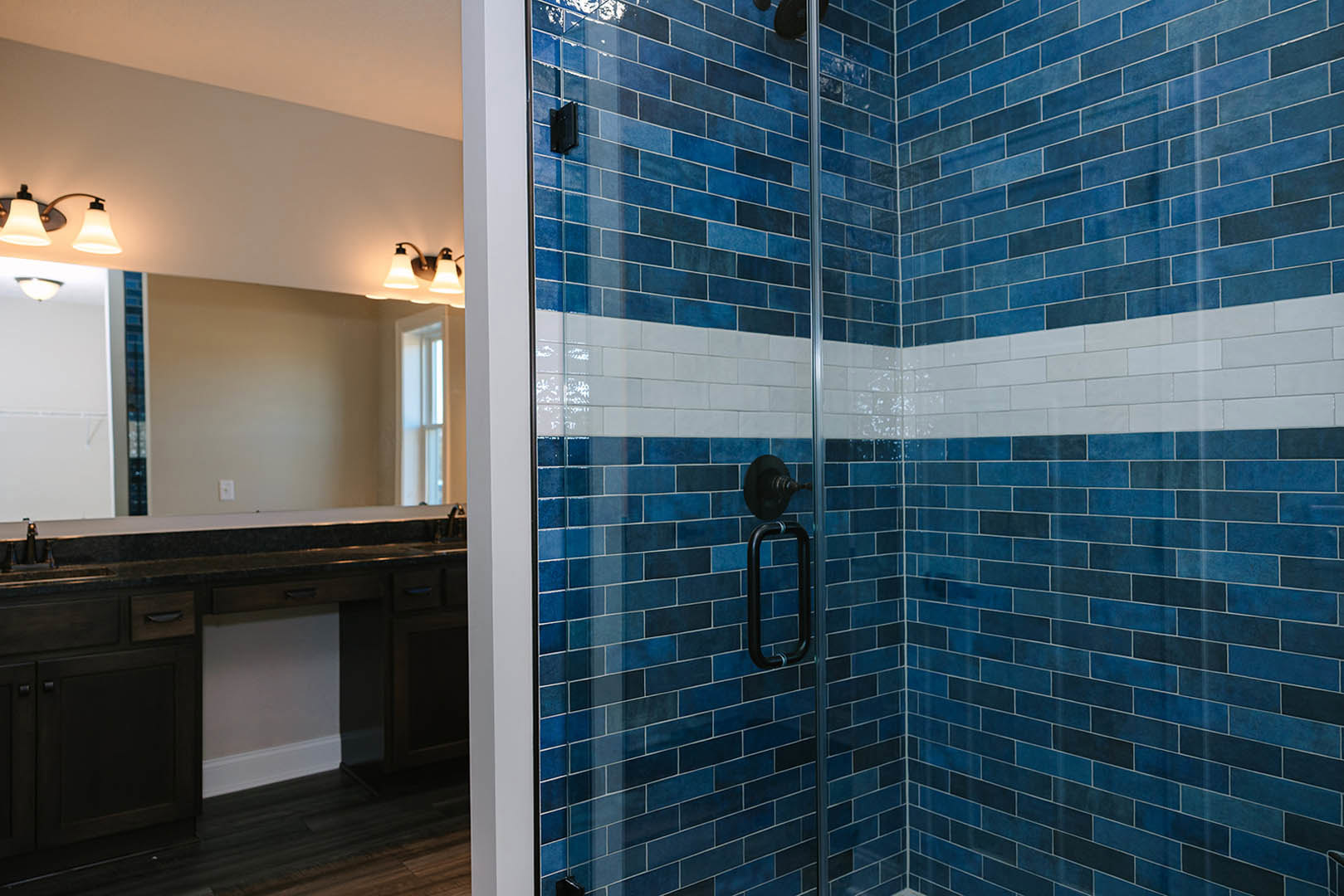Blue and white tiled shower with blue brick accent wall, black metal bars, white ceiling, and modern light fixture