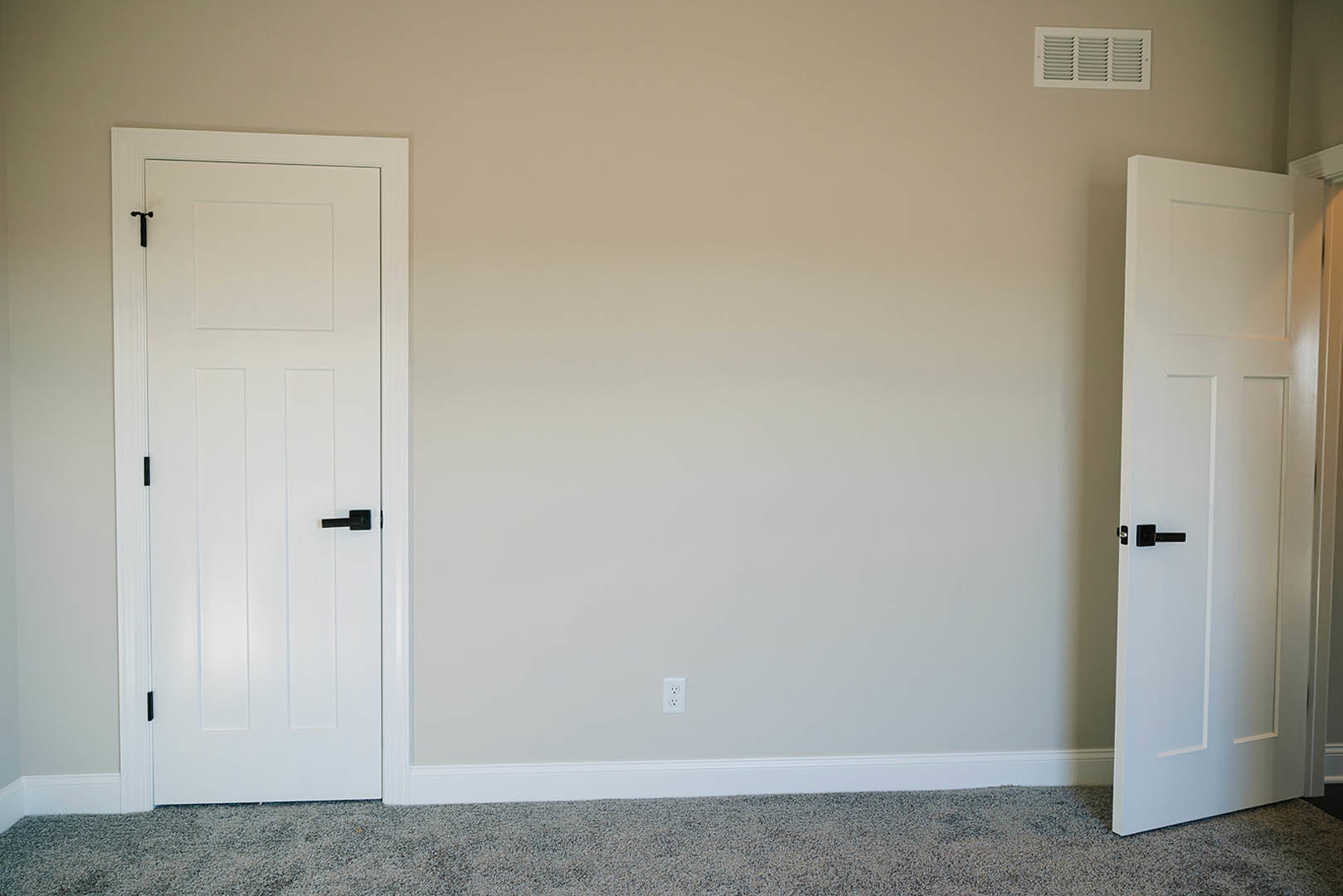 White paneled door with black handle set in a white wall, rectangular vent below, light-colored flooring