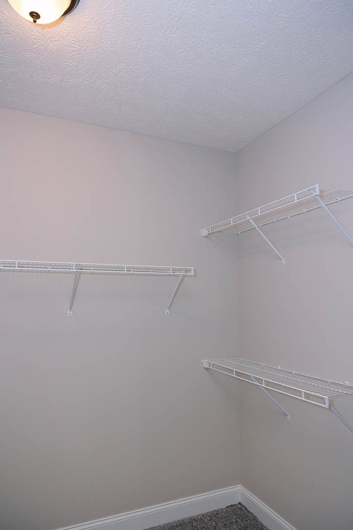 White built-in shelves mounted on a plaster wall above grey carpet, with a ceiling light fixture visible in a modern bathroom interior.