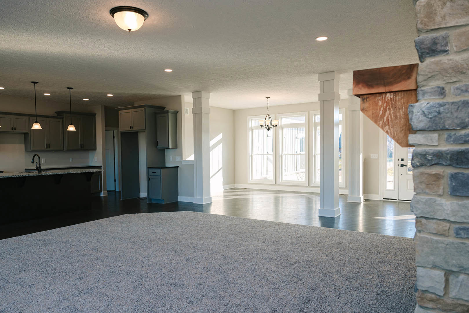 Open kitchen with stainless stove, exposed brick accent wall, white pillar with mounted light, carpeted flooring, and ceiling light fixture.