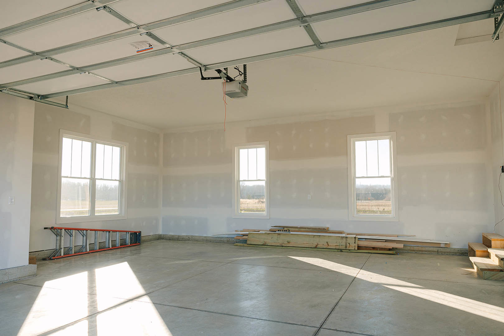 Spacious room featuring multiple large windows with white frames, plaster walls, light-colored concrete floor, and a high ceiling allowing abundant daylight