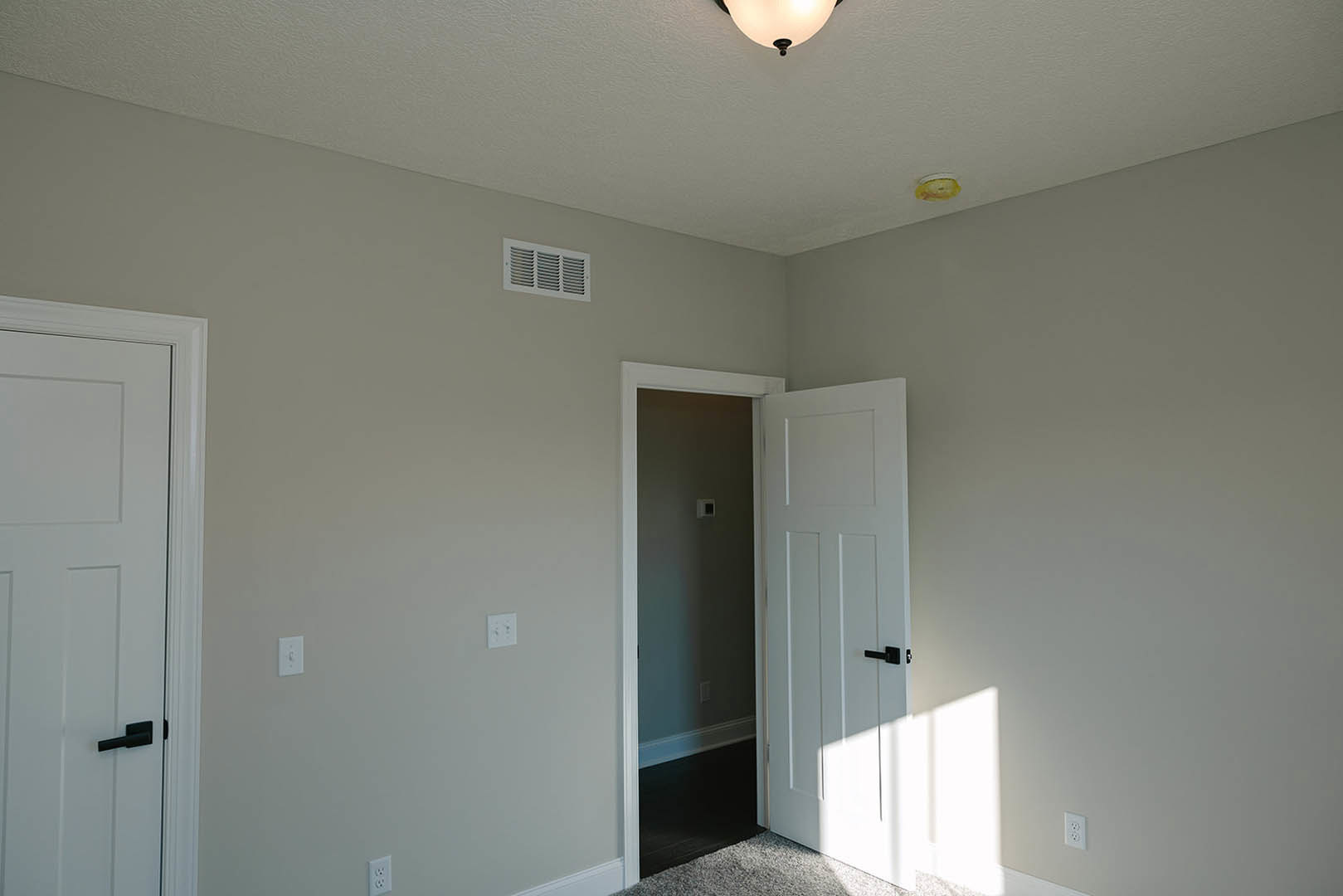 White paneled door with matte black handle set in a plaster wall, ceiling vent and recessed light visible above, light wood flooring below