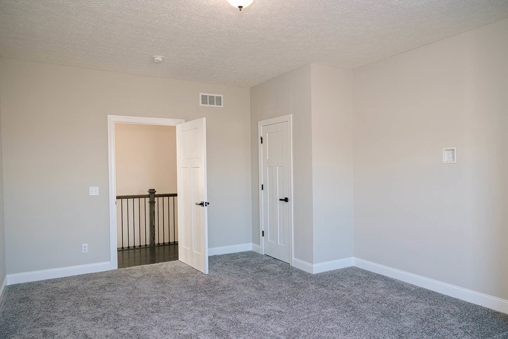 Room with two white doors, carpeted walls, white electrical outlet, white molding, and neutral carpet flooring
