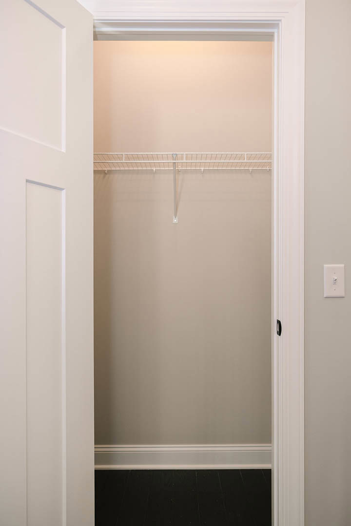 Walk-in closet with white shelf, white walls, light switch, and white metal railing; black tile with white border visible on floor
