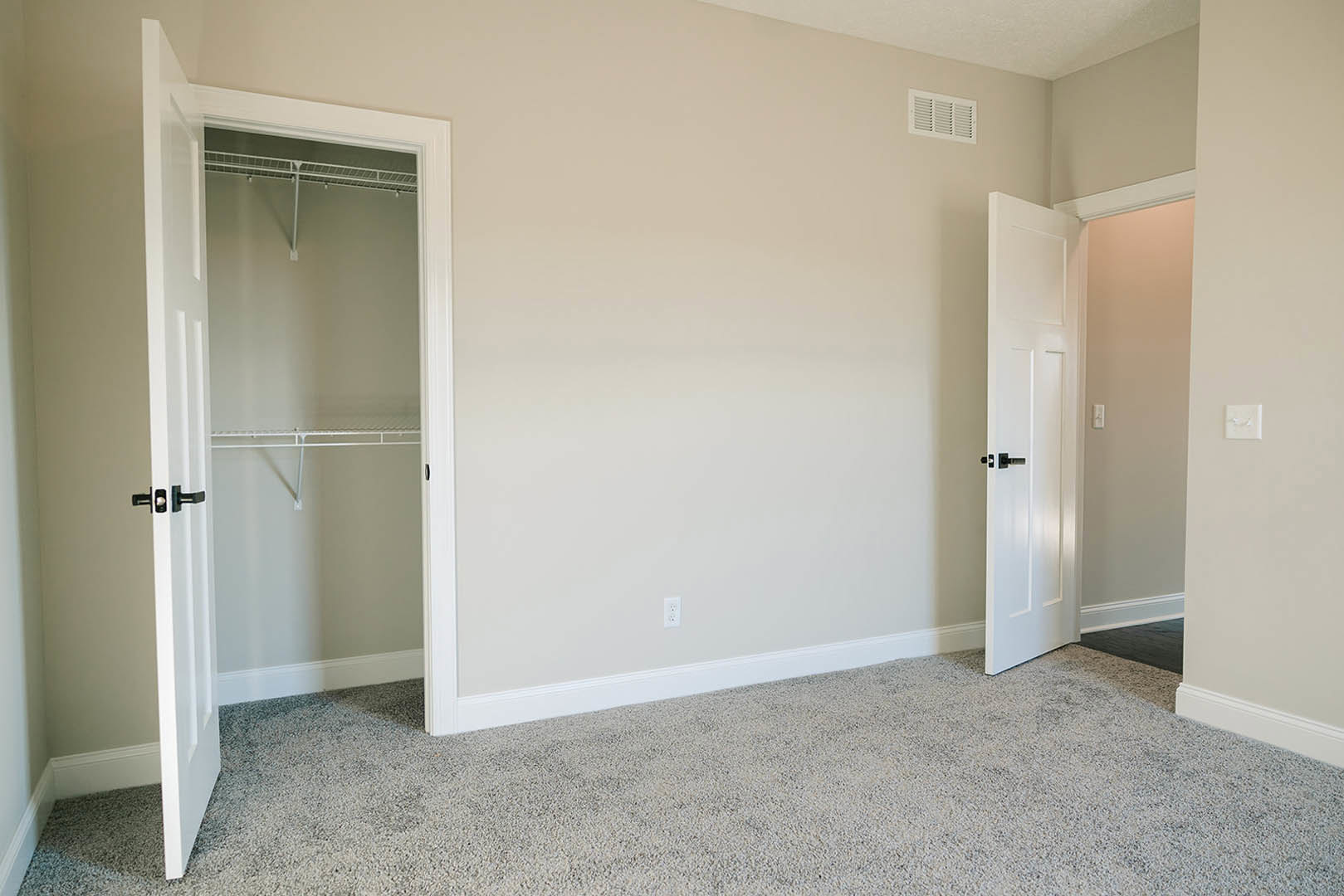 Bedroom with white carpet, white closet featuring built-in shelf, white door, wall-mounted light switch, and air vent on pale painted wall