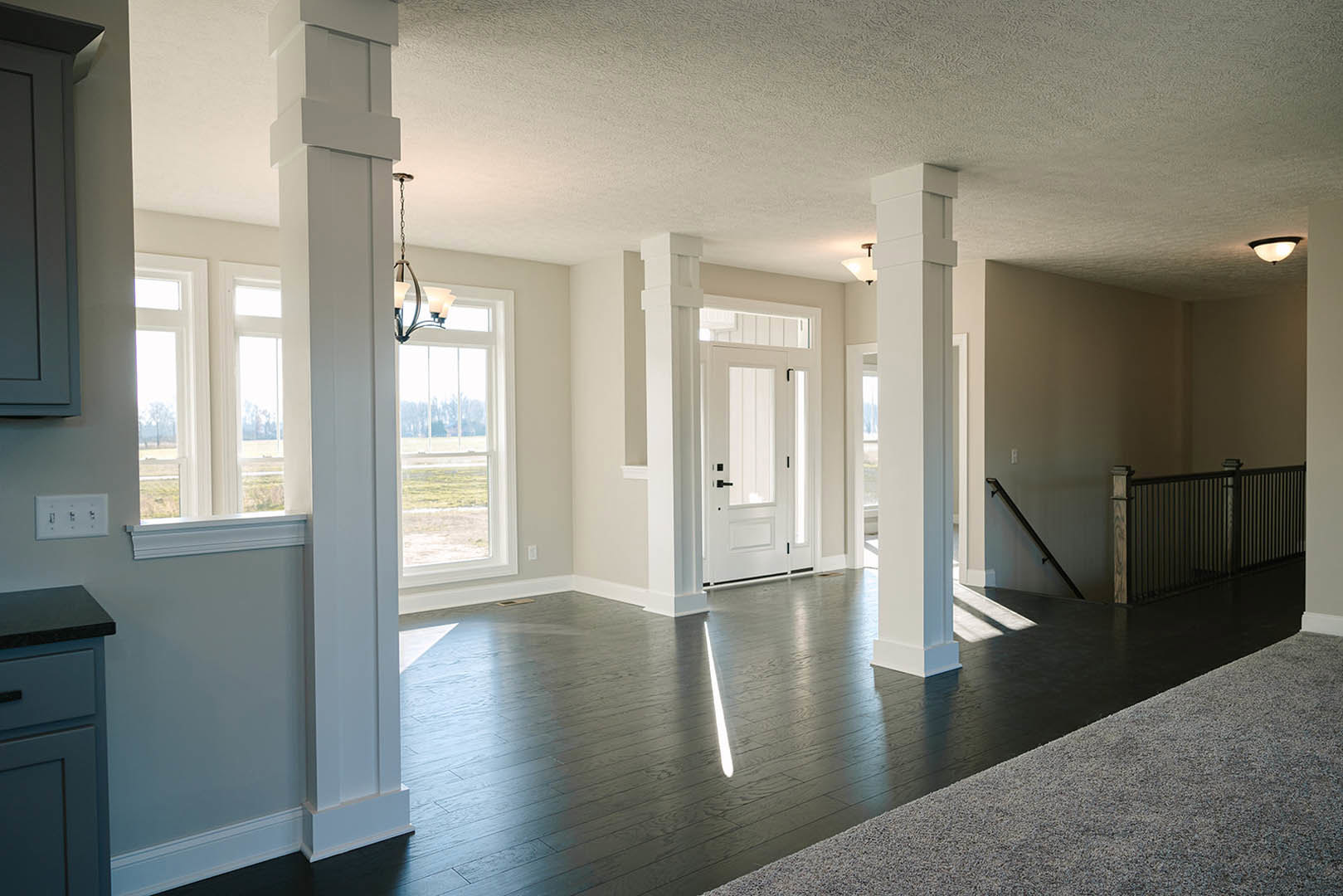 Kitchen with white pillars, light plaster walls, wood flooring, black metal fence, white wall outlet with multiple switches, white cabinetry, and a paneled door