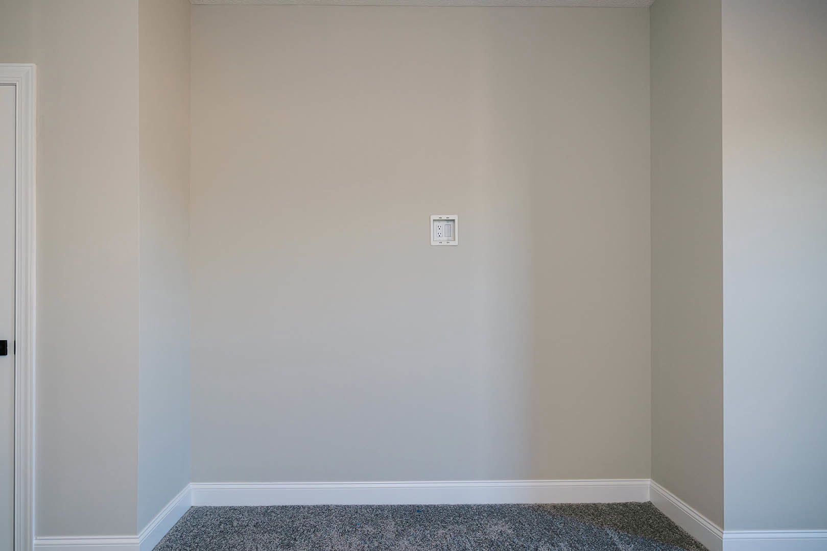 White painted wall with a modern light switch, adjacent to a white door frame and handle, smooth plaster finish and subtle molding detail.