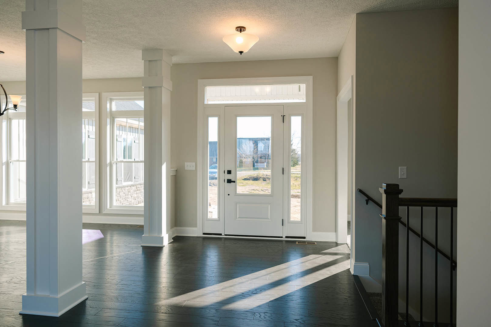 Hallway featuring dark wood flooring, white columns, white doors with glass panes, windows, and a ceiling light fixture