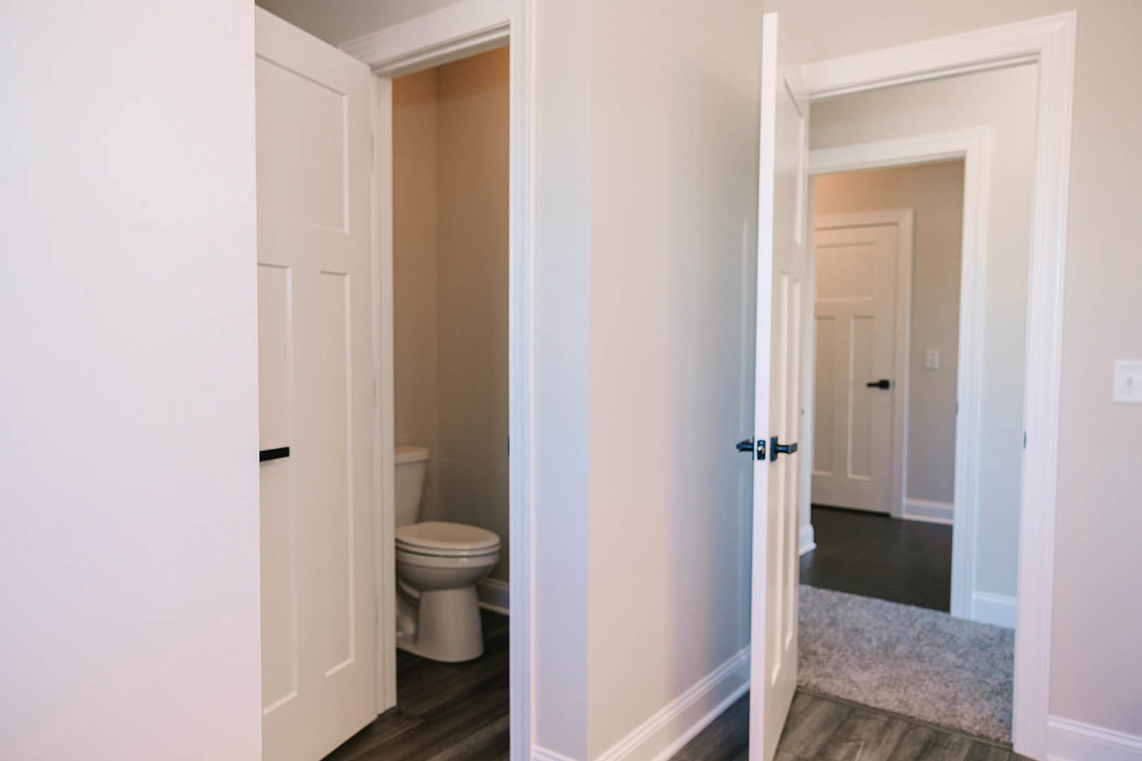 Bathroom with white walls, white door featuring black handles, toilet, light tile flooring, and minimal decor